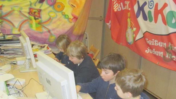 Eine Gruppe Kinder sitzt an Computern vor einem farbenfrohen Hintergrund.