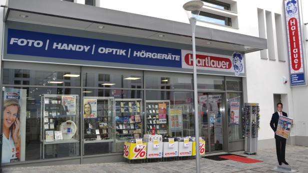 Die Fassade eines Hartlauer-Geschäfts mit Werbung für Foto, Handy, Optik und Hörgeräte.