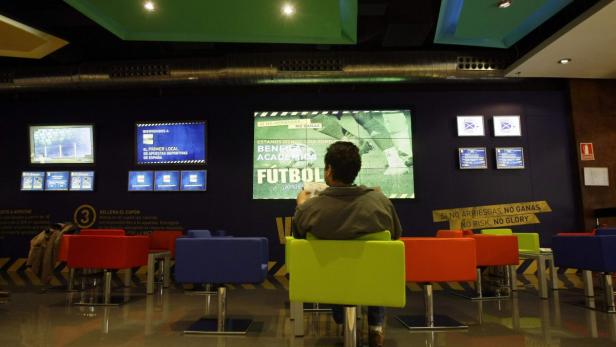 A man reads a newspaper and watches the screens in Spain&#039;s first sports betting shop in Madrid, April 17, 2008. The shop opened for business on Wednesday, one of thousands that foreign bookmakers hope to launch in the football-crazy nation which already bets more than any other European country.REUTERS/Andrea Comas (SPAIN)
