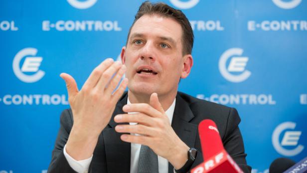Ein Mann in einem Anzug gestikuliert vor einem blauen Hintergrund mit dem E-Control Logo.