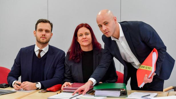 Drei Personen sitzen an einem Tisch mit Dokumenten und Ordnern.