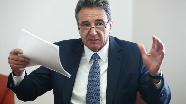 Ein Mann im Anzug gestikuliert mit einem Blatt Papier in der Hand.