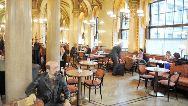 Innenansicht des Café Central in Wien mit Gästen und einer Statue von Peter Altenberg.