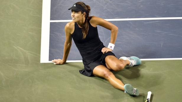Eine Tennisspielerin sitzt erschöpft auf dem Platz.