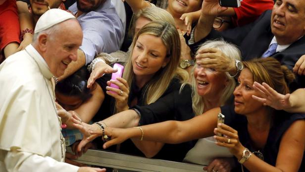 Papst Franziskus interagiert mit einer Menschenmenge, die Handys zum Fotografieren bereithält.