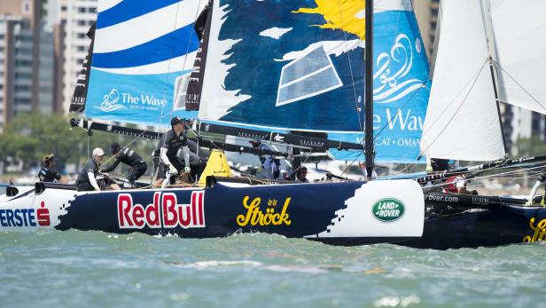 Ein Segelboot mit dem Red Bull-Logo und mehreren Seglern an Bord fährt auf dem Wasser.