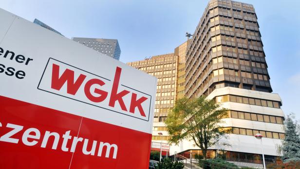 Ein Schild mit dem WGKK-Logo vor einem Bürogebäude.