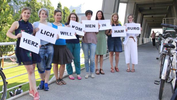 Eine Gruppe von Frauen hält Schilder mit der Aufschrift „Herzlich Willkommen in Hamburg“.