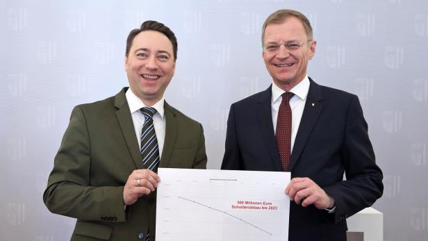 Zwei Männer im Anzug präsentieren eine Grafik zum Schuldenabbau bis 2023.