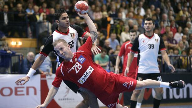 Ein Handballspieler wirft den Ball, während ein Gegenspieler ihn zu blocken versucht.