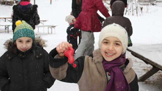 Zwei Mädchen spielen im Schnee mit einem roten Spielzeug.