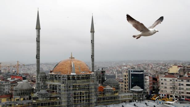 A seagull flies over the Taksim sqaure with a new mosque under construction in the background, in central Istanbul