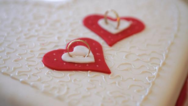 Zwei rote Herzen mit Eheringen auf einer Hochzeitstorte.