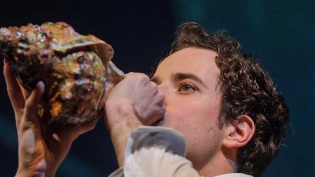 Ein Mann mit lockigem Haar bläst in ein großes Schneckenhorn.