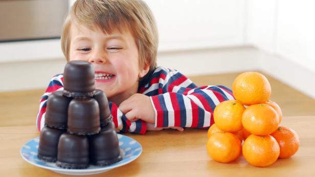 Ein Junge freut sich über einen Teller Schokoküsse und einen Stapel Mandarinen.
