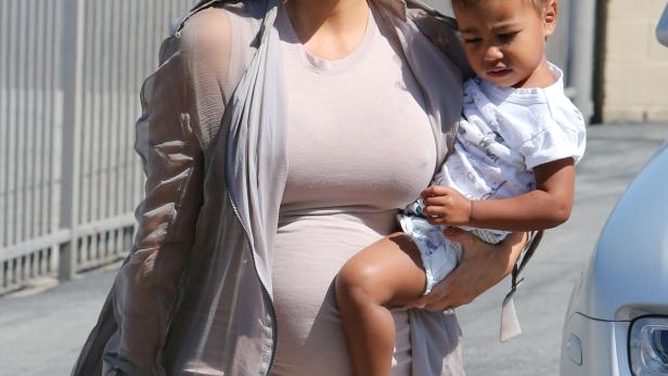 Kim Kardashian trägt ihr Kind, während sie eine Handtasche und Geschenke hält.