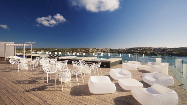 Eine Dachterrasse mit weißen Stühlen, Liegen und Whirlpools bietet einen Blick auf das Meer.
