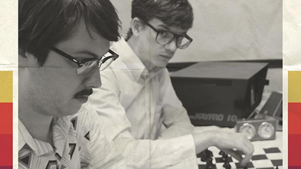 Zwei Männer spielen Schach; ein Kaypro 10 Computer steht im Hintergrund.