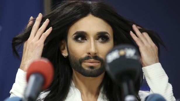 Conchita Wurst posiert vor Mikrofonen und fährt sich mit den Händen durch die Haare.