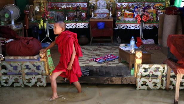 Ein junger buddhistischer Mönch watet durch das Wasser in einem Raum voller religiöser Gegenstände.