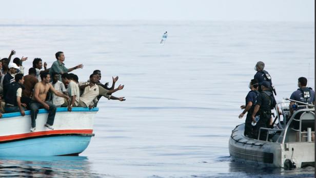 Ein Boot voller Menschen streckt die Hände nach einer Wasserflasche aus, die von einem anderen Boot geworfen wird.