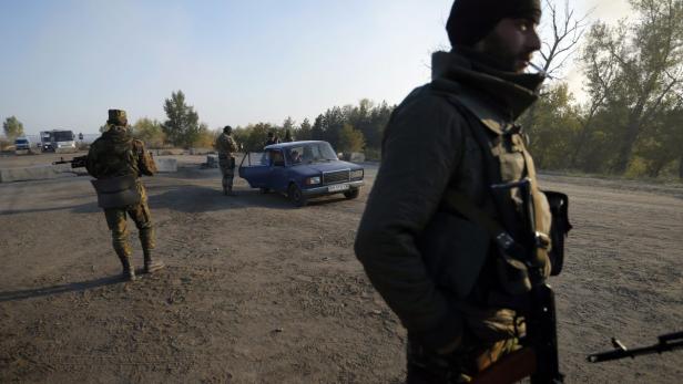 Bewaffnete Soldaten kontrollieren ein blaues Auto an einem Kontrollpunkt.