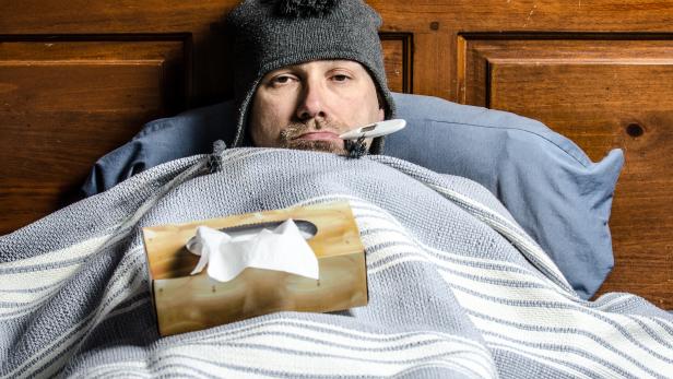 man sick in bed with a thermometer in his mouth