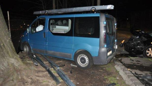 Ein blauer Lieferwagen ist gegen einen Baum gefahren, im Hintergrund ein beschädigtes Auto.
