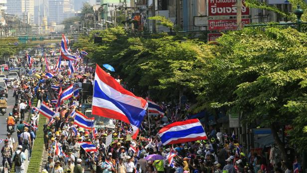 Eine Menschenmenge demonstriert mit thailändischen Flaggen in einer Stadt.