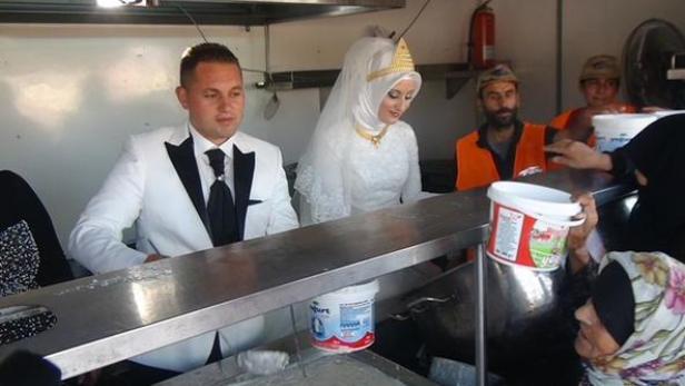 Ein Brautpaar in traditioneller Kleidung steht an einem Tresen und verteilt Joghurt.