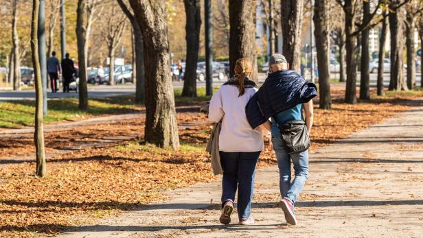 Ein Paar geht im Herbst durch einen Park mit vielen Bäumen und Laub.