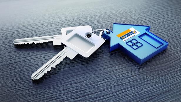Zwei Schlüssel liegen neben einem blauen Schlüsselanhänger in Hausform von Faircheck Immoservice.