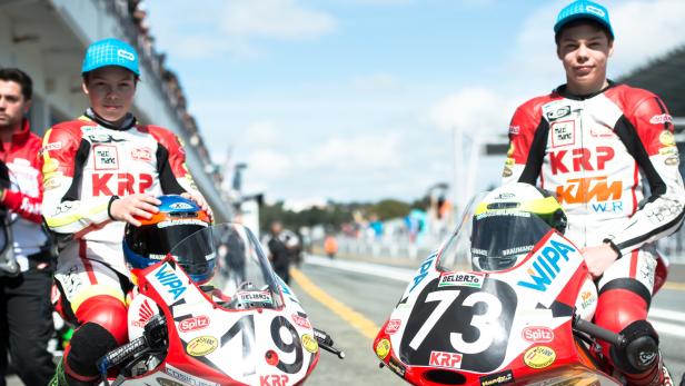 Zwei junge Rennfahrer sitzen auf ihren Motorrädern mit den Nummern 19 und 73.