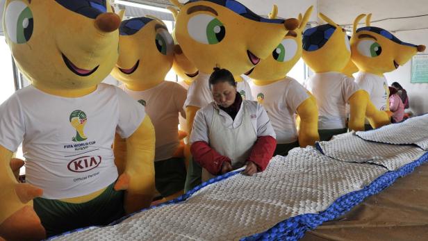 Eine Frau arbeitet an einer Matte vor einer Reihe von Fuleco-Maskottchen der FIFA Fussball-Weltmeisterschaft 2014.