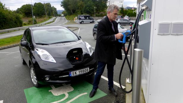 Ein Mann lädt ein schwarzes Elektroauto an einer Ladestation auf.