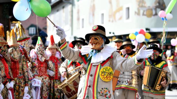 Eine Gruppe von Menschen in traditionellen Narrenkostümen feiert Fasching mit Musik und bunten Luftballons.