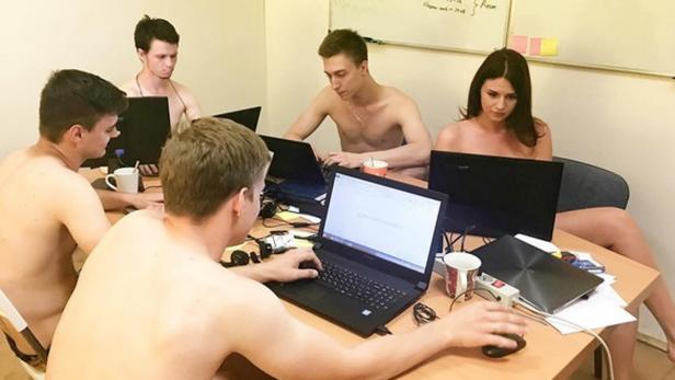 Eine Gruppe von oben ohne gekleideten Personen sitzt an einem Tisch und arbeitet an Laptops.