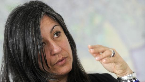 Eine Frau mit dunklen Haaren und silbernen Strähnen gestikuliert mit der Hand.