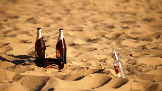 Mehrere leere Bier- und Wodkaflaschen liegen im Sand.