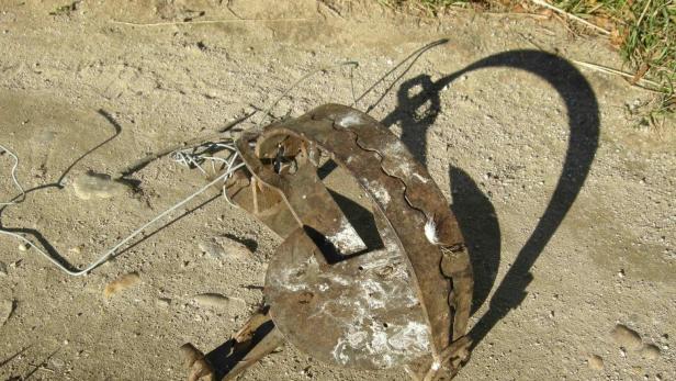 Eine alte, rostige Tierfalle liegt auf sandigem Boden.