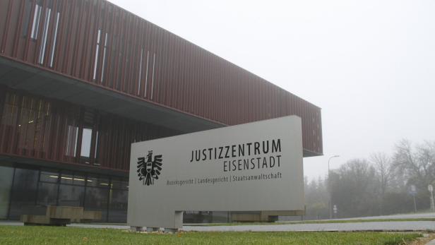 Modernes Justizzentrum mit großem Schild und Rasenfläche im Vordergrund, dahinter nebliges Wetter und Bäume.