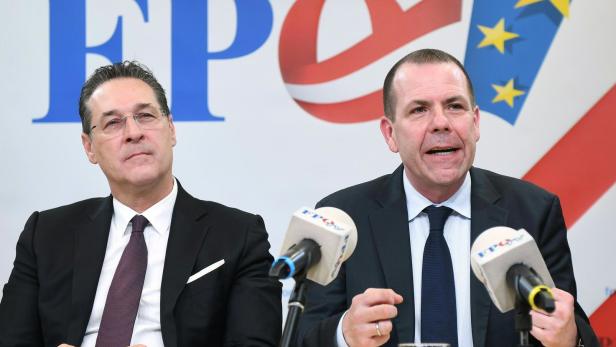 Zwei Männer in Anzügen sitzen vor einem FPÖ-Logo an einem Tisch mit Mikrofonen.