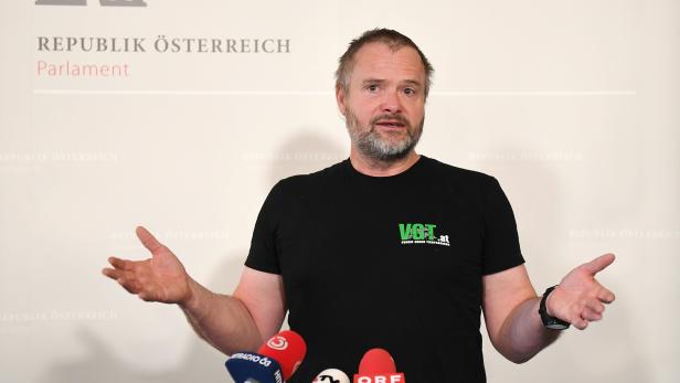Ein Mann vom VGT steht vor Mikrofonen im österreichischen Parlament und gestikuliert.