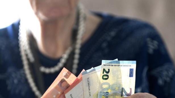 Eine ältere Frau mit Brille und Perlenkette hält Euro-Banknoten in der Hand.