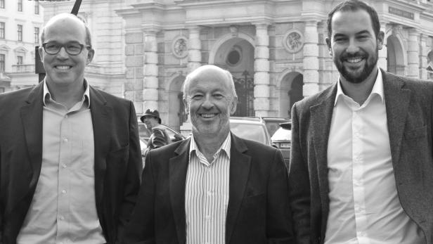 Drei lächelnde Männer in Anzügen stehen vor einem Gebäude.