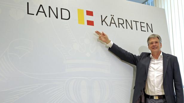 Ein Mann in Anzug präsentiert das Logo des Landes Kärnten.