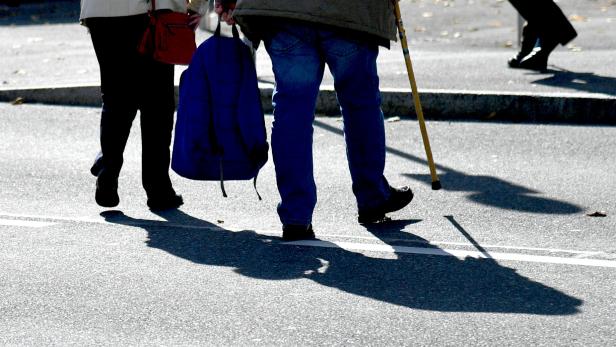Pensionäre gehen mit einem Stock und einer blauen Jacke über eine Straße.