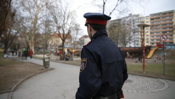 Ein Polizist steht in einem Park mit Spielplatz im Hintergrund.