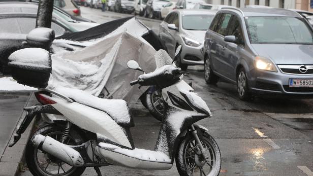 Ein schneebedeckter Motorroller steht auf einer nassen Straße.