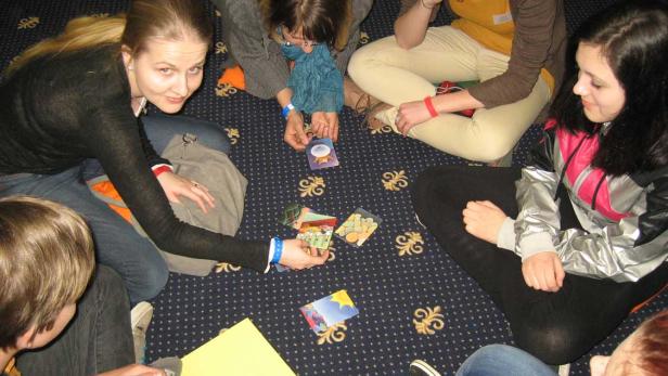 Eine Gruppe junger Leute sitzt auf dem Boden und spielt Karten.
